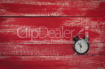 Small black clock on a worn red wooden surface