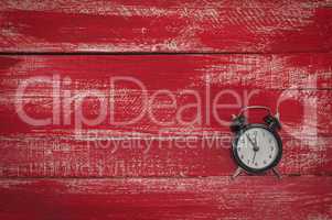 Small black clock on a worn red wooden surface