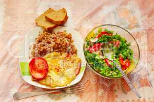 dish for a dinner from boiled buckwheat sausage fried eggs and fresh vegetables