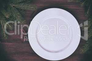 White empty plate with a green branch of spruce on a wooden surf