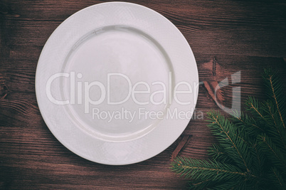 White empty plate with a green branch of spruce on a wooden surf