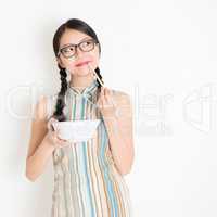 Oriental girl eating with chopsticks and thinking