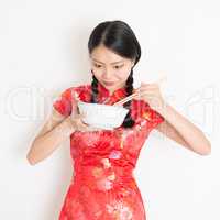 Oriental girl in red cheongsam eating with chopsticks