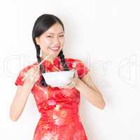 Oriental woman in red cheongsam eating with chopsticks