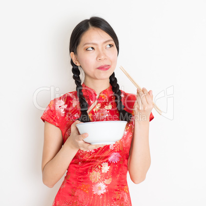 Oriental girl in red qipao eating with chopsticks