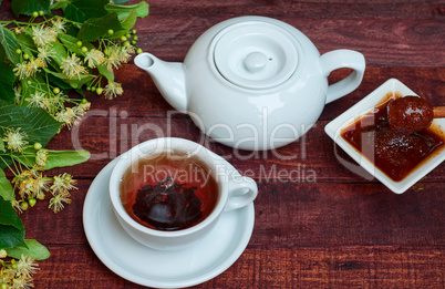 White cup of hot black tea, teapot and honey of linden tree