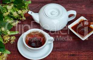 White cup of hot black tea, teapot and honey of linden tree