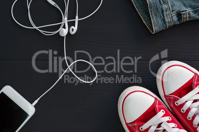 Smartphone with headphones and red sneakers on a black wooden su