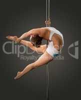 Young sexy brunette poledancer on pylon in studio