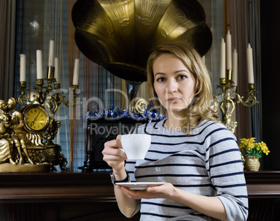 portrait of a young woman stends near the fireplace, happy smiling girl drinks tea