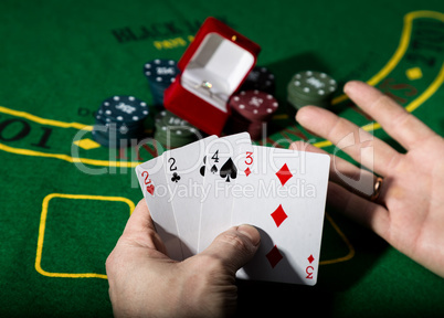 casino chips and a precious ring on green poker table background, man holding losing combination of cards