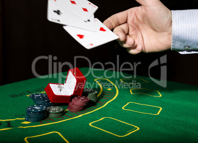 casino chips and a precious ring on green poker table background, man throws cards with losing combination.