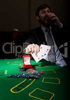 gambling addiction. man in a business suit drinking brandy and throws cards with losing combination. casino chips, precious ring on green poker table