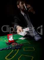 gambling addiction. man in a business suit drinking brandy and throws cards with losing combination. casino chips, precious ring on green poker table