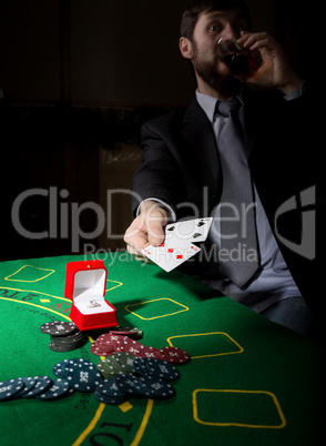 gambling addiction. man in a business suit drinking brandy and throws cards with losing combination. casino chips, precious ring on green poker table