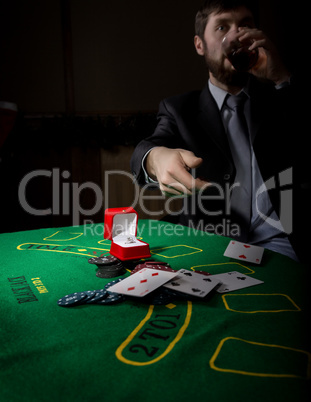 gambling addiction. man in a business suit drinking brandy and throws cards with losing combination. casino chips, precious ring on green poker table