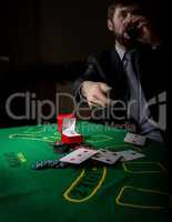 gambling addiction. man in a business suit drinking brandy and throws cards with losing combination. casino chips, precious ring on green poker table