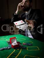 gambling addiction. man in a business suit drinking brandy and throws cards with losing combination. casino chips, precious ring on green poker table