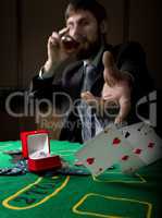 gambling addiction. man in a business suit drinking brandy and throws cards with losing combination. casino chips, precious ring on green poker table