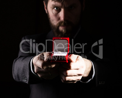 bearded man in business suit gives a ring in the red box and expresses different emotions on dark background