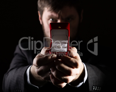 bearded man in business suit gives a ring in the red box and expresses different emotions on dark background