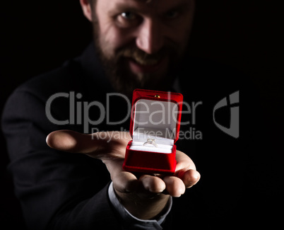 bearded man in business suit gives a ring in the red box and expresses different emotions on dark background