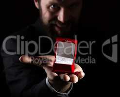 bearded man in business suit gives a ring in the red box and expresses different emotions on dark background