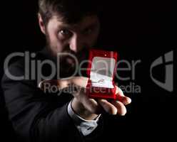 bearded man in business suit gives a ring in the red box and expresses different emotions on dark background