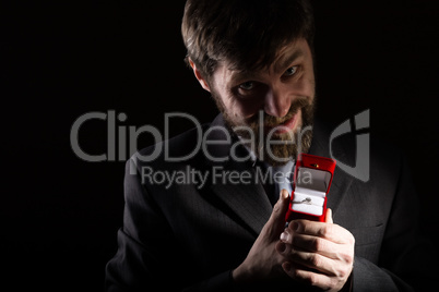 bearded man in business suit gives a ring in the red box and expresses different emotions on dark background