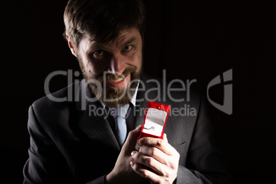 bearded man in business suit gives a ring in the red box and expresses different emotions on dark background