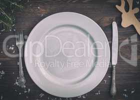 White plate with silver knife and fork on brown wooden surface C