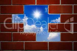 Brick wall and blue sky with clouds and sun.
