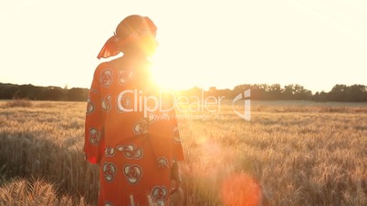 African woman in traditional clothes standing in a field of crops at sunset or sunrise