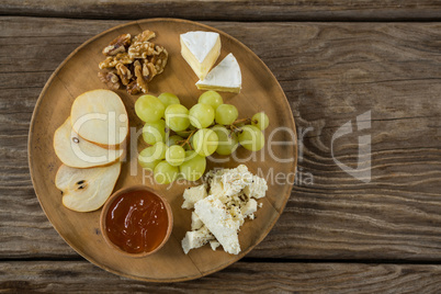 Cheese with grapes, apple slices, walnuts and sauce on wooden plate