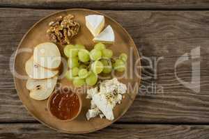 Cheese with grapes, apple slices, walnuts and sauce on wooden plate