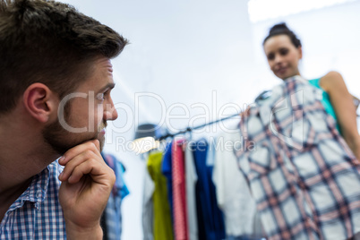 Bored man with shopping bags while woman by clothes rack