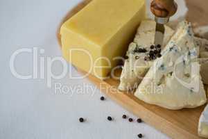 Variety of cheese with black pepper and knife on wooden board