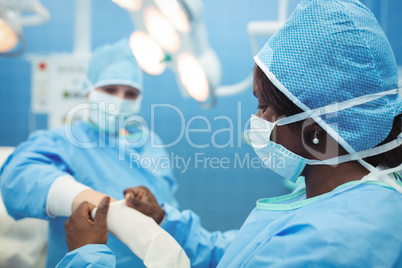 Female surgeon helping her co-worker in wearing surgical gloves