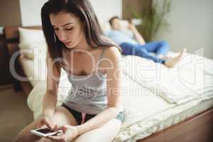 Woman using mobile phone while man sleeping on bed