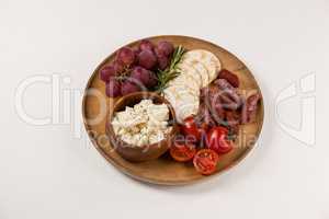 Crispy biscuits, cherry tomatoes, grapes and bowl of cheese on wooden board