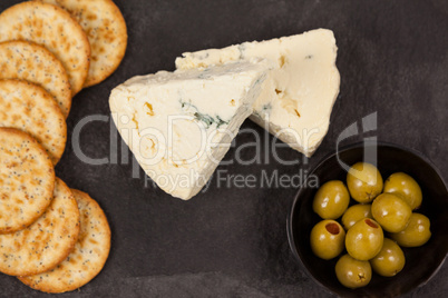 Crispy biscuits, cheese and bowl of green olives on chopping board