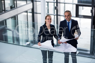 Portrait of business colleagues standing with blueprint in corridor