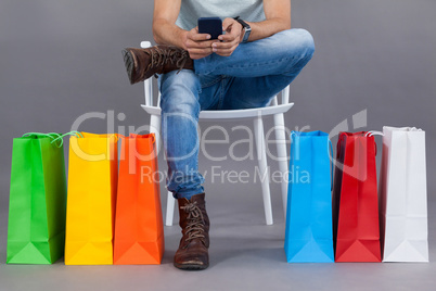 Man sitting on a chair with colorful shopping bags and using mobile phone