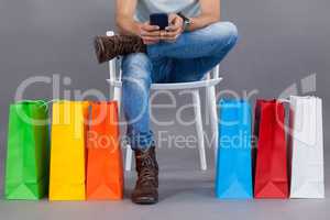 Man sitting on a chair with colorful shopping bags and using mobile phone