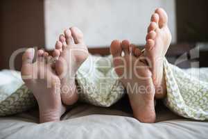 Couple showing their feet while lying on a bed