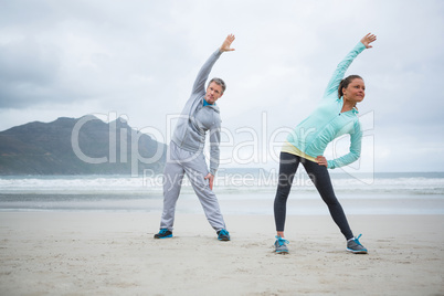 Couple performing stretching exercise on beach