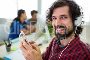 Portrait of smiling business executive listening to music on mobile phone