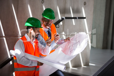 Architects standing on a staircase discussing with blueprint