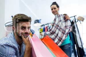 Bored man with shopping bags while woman by clothes rack