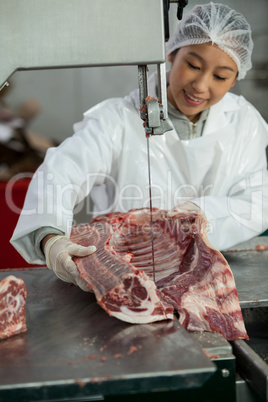 Female butcher cutting raw meat on a band saw machine